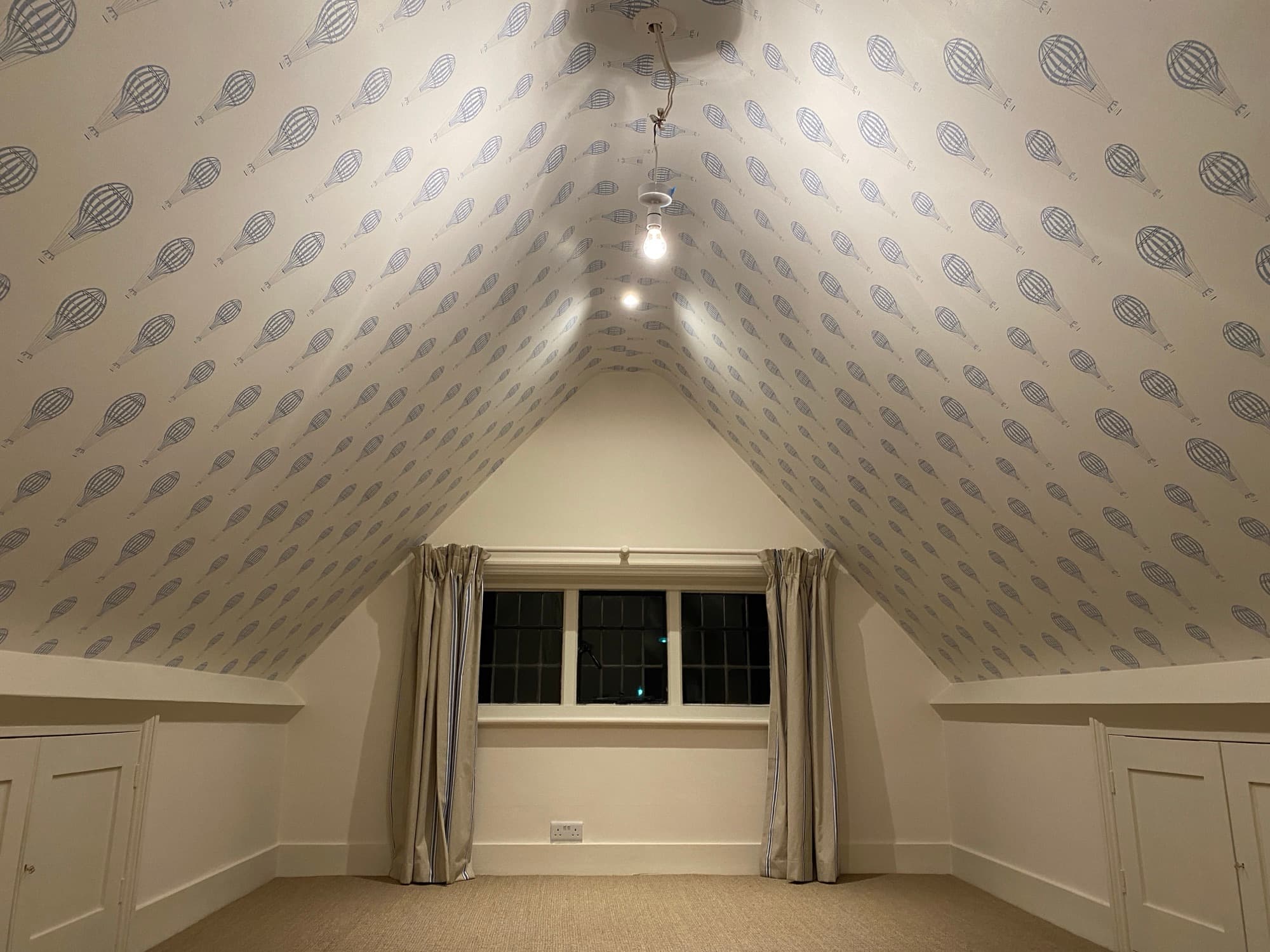Same loft bedroom finished with hot air balloon print wallpaper pattern-matched across the vaulted ceiling
