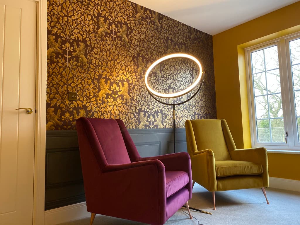 Finished room with a gold damask wallpaper feature wall, painted wall panelling below the dado rail, and two velvet armchairs